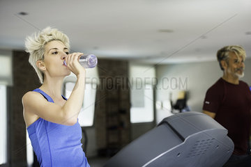 Woman drinking water while exercising on treadmill