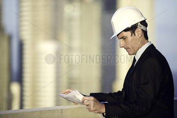 Man wearing hard hat outdoors reviewing blueprint