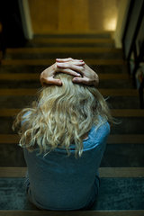 Woman sitting on stairs with hands clasped on head  rear view