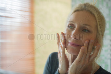 Mature woman looking at her reflection in mirror with hands on cheeks