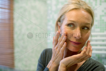 Mature woman looking at reflection in mirror with hand on cheek