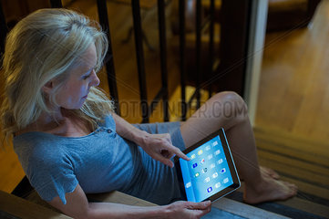 Mature woman sitting on stairs at home  using digital tablet