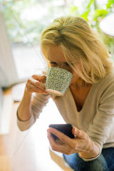 Woman drinking coffee and using smartphone at home