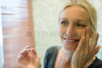 Mature woman looking at her reflection in mirror with hands on cheeks