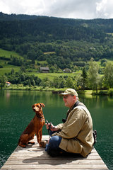 Feld am See  Oesterreich  Mann mit seinem Hund am Brennsee