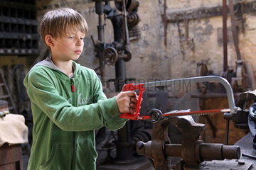 Cammin  Deutschland  Junge bearbeitet eine Eisenstange mit einer Saege
