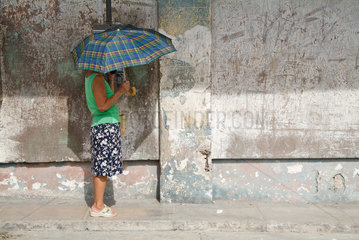 Havanna  Kuba  Frau mit Schirm steht an einem oeffentlichen Fernsprecher