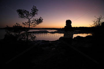 Vaestervik  Schweden  Silhouette  Kind sitzt in der Daemmerung allein an einem See