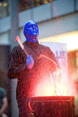 Berlin  Deutschland  ein Blue Man trommelt und verspritzt rote Farbe