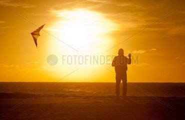 Stenbjerg  Daenemark  ein Mann laesst bei Sonnenuntergang einen Drachen steigen