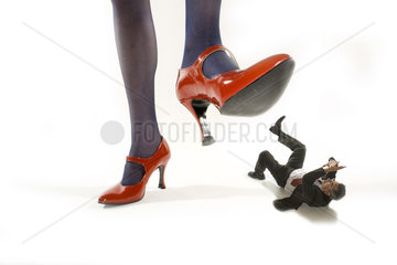 Frau in roten Stoeckelschuhen tritt auf winzigen Mann