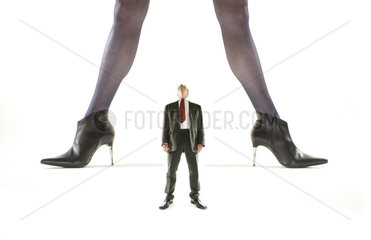 winziger Geschaeftsmann schaut nach oben zwischen die Beine einer riesigen Frau