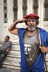 Havanna  Kuba  ein Strassenfeger mit einem Che-Shirt  Zigarre und roter Baskenmuetze salutiert
