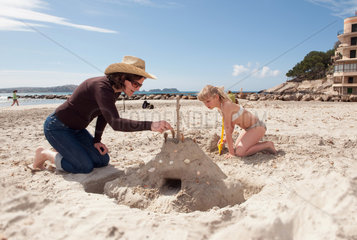 Peguera  Mallorca  Spanien  ein Maedchen baut mit ihrer Mutter eine Sandburg