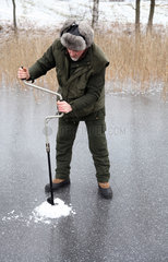 Belloe  Schweden  Mann bohrt ein Loch fuer das Eisfischen in den See Stora Bellen