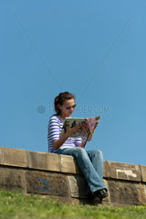 Krakau  Polen  eine junge Frau sitzt auf einer Mauer an der Weichsel und liest
