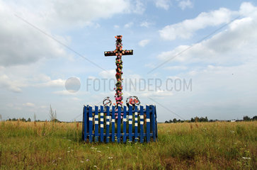 Wadol  Weissrussland  freistehendes Kreuz geschmueckt mit Plastikblumen auf einer Wiese