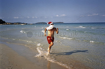 Weihnachtsmann in Badehose joggt am Strand