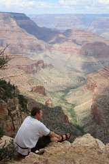 Flagstaff  USA  ein Tourist geniesst sitzend den Ausblick in den Grand Canyon
