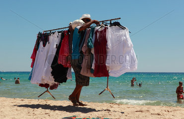 Santa Margherita di Pula  Italien  Mann traegt eine Kleiderstange mit T-Shirts am Strand entlang