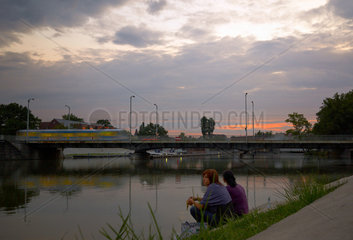 Breslau  Polen  zwei Frauen sitzen in der Abenddaemmerung am Ufer der Oder