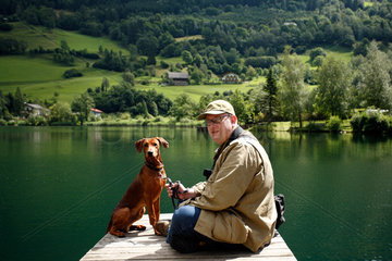 Feld am See  Oesterreich  Mann mit seinem Hund am Brennsee