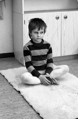 Berlin  DDR  ein kleiner Junge sitzt im Kindergarten verunsichert im Schneidersitz auf dem Boden