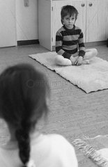 Berlin  DDR  ein kleiner Junge sitzt im Kindergarten gelangweilt im Schneidersitz auf dem Boden