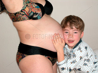 Junge horcht am Bauch seiner schwangeren Mutter