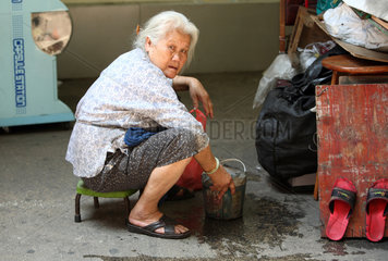 Macau  China  alte Frau sitzt mit einem Wassereimer auf der Strasse