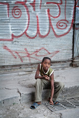 Havanna  Kuba  ein Junge sitzt auf dem Buergersteig in Alt-Havanna