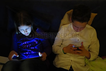 Berlin  Deutschland  Jugendliche schauen im Dunkeln auf ihre Bildschirme von Smartphone und Tablet-PC