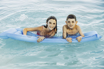 Smiling brother and sister swimming with inflatable