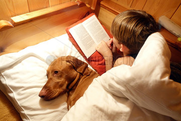 Krippenbrunn  Oesterreich  Junge liegt mit seinem Hund im Bett und liest in einem Buch