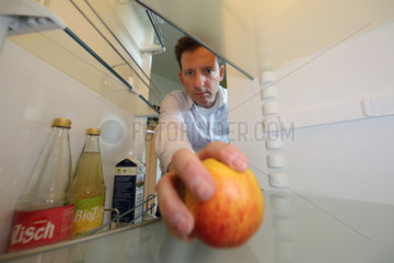 Berlin  Deutschland  Mann holt einen Apfel aus seinem fast leeren Kuehlschrank