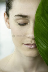 Young woman holding large leaf over half of her face  portrait