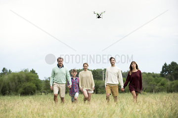 Family walking togther in field while drone flies overhead