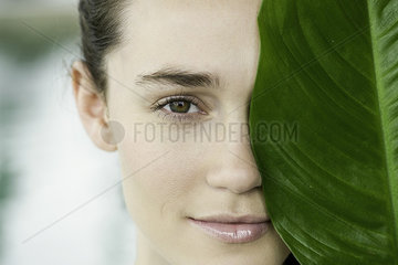 Young woman holding large leaf in front of her face and smiling