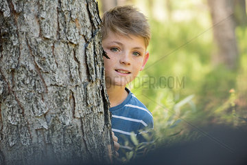 Boy peeking around tree trunk  portrait