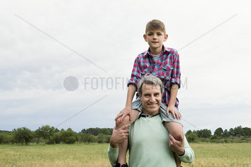 Grandfather carrying grandson on shoulders outdoors