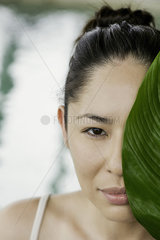Young woman holding large leaf in front of her face and smiling