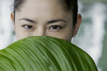 Young woman holding large leaf in front of her face