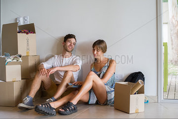 Young couple sitting in new house surrounded by cardboard boxes