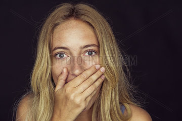 Young woman with wide eyes and hand covering mouth