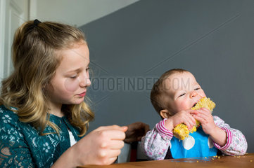 Berlin  Deutschland  16 Monate altes Baby isst einen Maiskolben  daneben ihre grosse Schwester