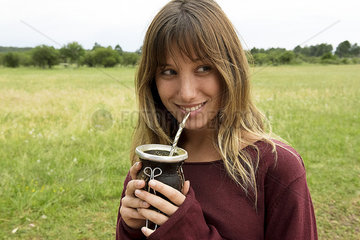 Young woman drinking yerba mate from gourd outdoors