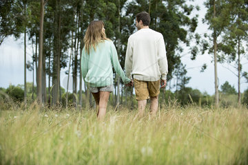 Young couple walking and holding hands outdoors  rear view