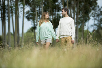 Young couple walking hand in hand through tall grass