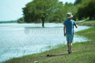 Boy walking along lake shore with fishing rod  rear view