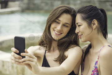 Women wearing bathing suits relaxing next to swimming pool posing for selfie